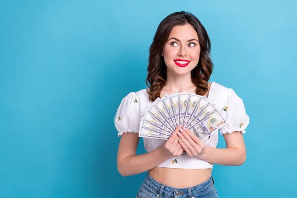 Photo of gorgeous positive minded girl hold dollar bills banknotes look empty space isolated on blue color background.