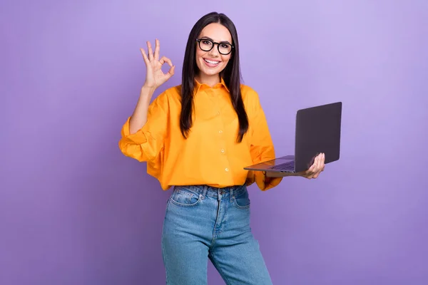 若い労働者の女性の写真オレンジのシャツを保持ノートパソコンを示すキーシンボルは 紫の色の背景に隔離された仕事をお勧めします — ストック写真