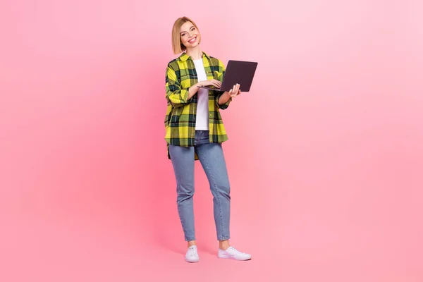 魅力的な若い女性のフル長さの写真は デバイスのラップトップを保持する服スタイリッシュなチェックイエロー衣装ピンク色の背景に隔離 — ストック写真