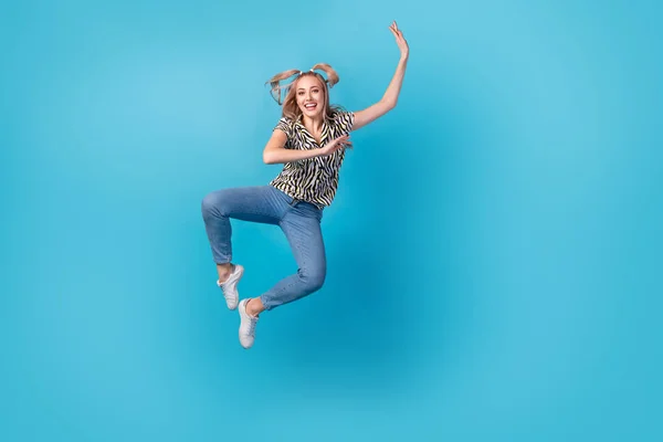 全长照片 满意的女孩穿着条纹衬衫裤子在空中手舞足蹈 与蓝色背景隔离 — 图库照片