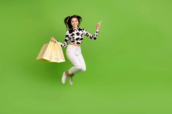 全长图片 滑稽女孩穿着牛仔皮的顶部跳跃高举购物者指向空旷的空间孤立的绿色背景 — 图库照片