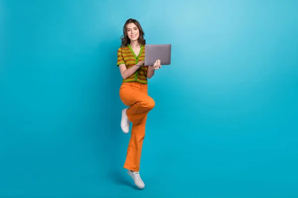 漂亮聪明的女孩穿着橙色裤子 色彩艳丽的羊毛衫 手持笔记本电脑发短信信 蓝色背景隔离的全长照片 — 图库照片