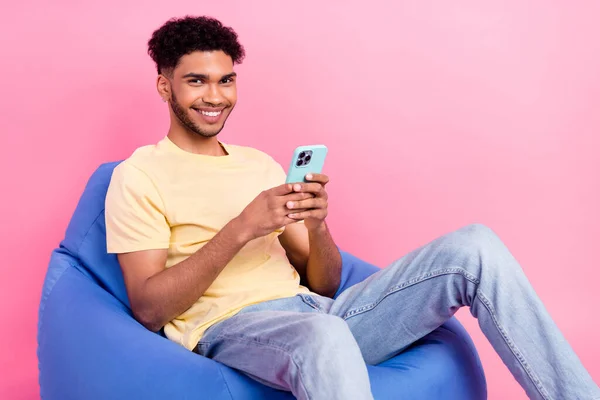 乐观积极的男人穿着黄色衬衫坐在书包上的全长照片 用粉色背景隔离的智能手机写一篇文章 — 图库照片