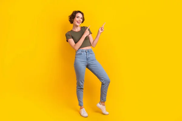 楽観的な女の子のフルサイズの写真は 黄色の色の背景に隔離された提供の空のスペースで示すカーキ色のTシャツデニムパンツを着用 — ストック写真