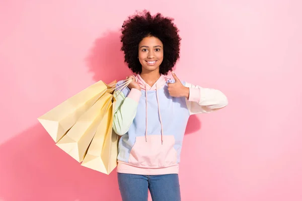 陽気な自信を持った小さな子供の写真は 親指が隔離されたピンク色の背景を示す買い物客を保持するスウェットシャツを着用します — ストック写真