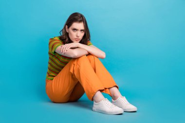 Full size photo of sad woman with wavy hairdo dressed colorful cardigan sit on floor looks offended isolated on blue color background. clipart