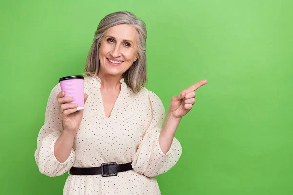 Photo of senior retired funny person with gray hair hold cup directing at proposition empty space isolated on green color background.