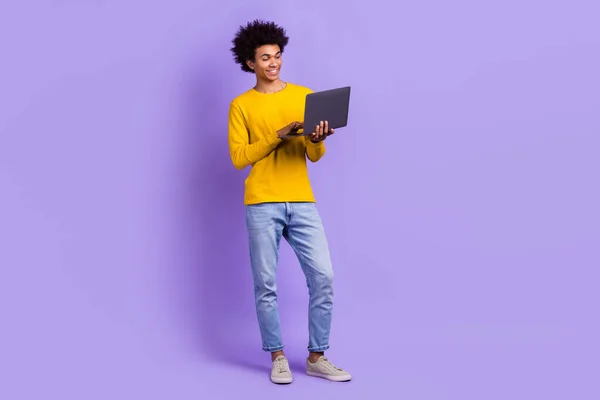 快適なフレンドリーな男のフルサイズの写真 黄色の長袖デニムパンツ 紫色の背景で隔離されたラップトップ上の電子メールを入力します — ストック写真