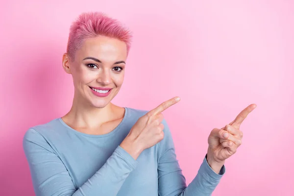 陽気なクールな女性の写真は ピンク色の背景を隔離された2本の指の空のスペースを指すブルーシャツを噛むリップを着用します — ストック写真