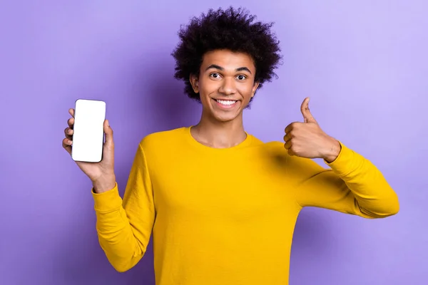 年轻小伙子穿着黄色衬衫的照片有着可笑的剪发大拇指 享受着新手机在紫色背景下的显示质量 — 图库照片