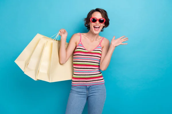 印象的なファンキーな女性の写真は 買い物客を隔離したブルーカラーの背景を保持するタンクトップダークアイウェアを着た — ストック写真