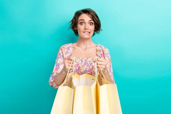 Portrait of worried nervous person hands hold mall boutique bags biting lips spent lot money isolated on turquoise color background.