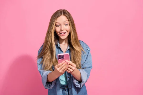 穿着时髦服装的积极快乐的女孩的画像用现代装置阅读以粉色背景为背景的有趣新闻 — 图库照片