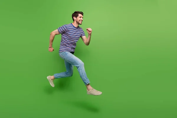 ワクワクするポジティブな男のフル長さの写真は 高速ジャンプするストライプTシャツを着用し 高空スペースを隔離された緑色の背景 — ストック写真