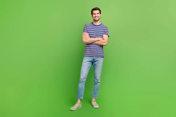 自信を持ってポジティブな男性の全長の写真は 隔離された緑色の背景を横断したストライプTシャツの腕を着用します — ストック写真