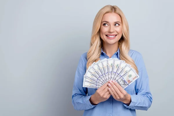 Portrait of minded positive elegant person toothy smile hold dollar bills look empty space isolated on grey color background.