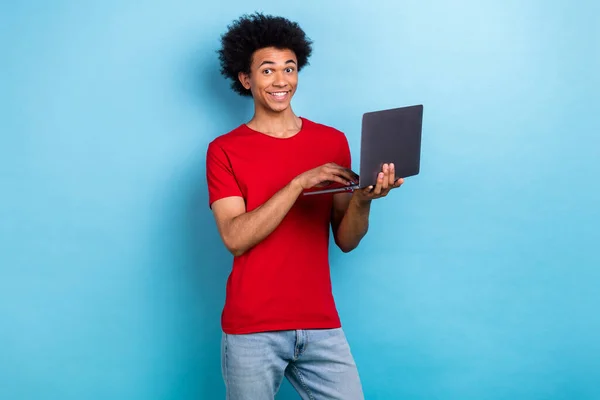良い気分ハンサムな男の写真 赤いスタイリッシュなTシャツ ブルーカラーの背景に隔離されたソーシャルメディアでノートパソコンのタイピングポストを保持 — ストック写真