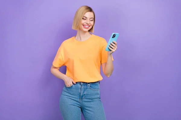 ボブヘアスタイルの可愛いおかしな女の子の写真は 黄色のTシャツを着用しています スマートフォンを見て 紫色の背景に隔離された電子メールを読む — ストック写真