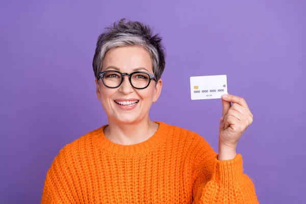 穿着橙色毛衣的短发女子满意的照片 手握紫色背景的信用卡 — 图库照片