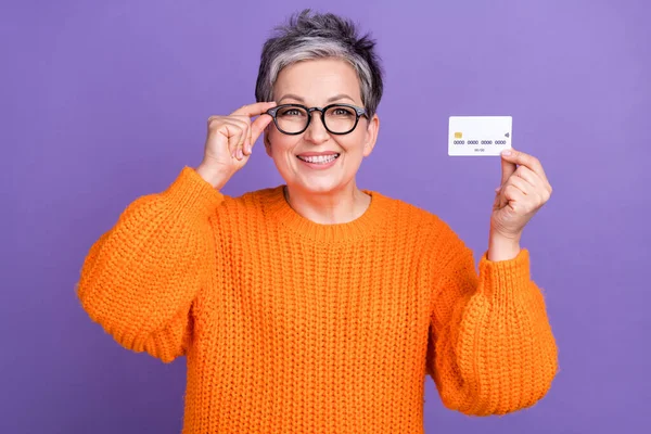 高级女商人拿着塑料借记卡广告大肆宣扬穿橙色套头衫 背景为紫色的照片 — 图库照片