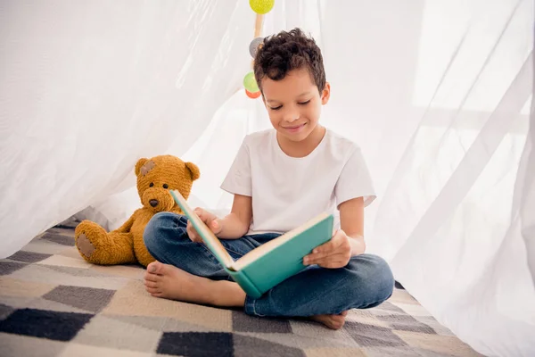 聪明的小男孩在家读书的照片在家里的野营游戏室里看有趣的课本 — 图库照片