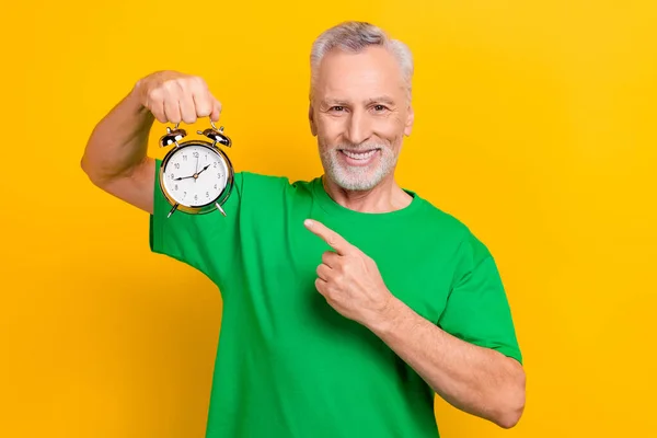 Portrait of positive friendly person direct finger arm hold retro classic bell ring clock isolated on yellow color background.