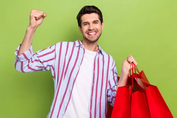 Photo of lucky overjoyed man with stubble dressed striped shirt raising fist up buy new clothes isolated on green color background.