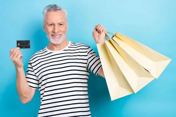 Photo portrait of nice elderly man hold shopping bags credit card dressed stylish striped outfit isolated on blue color background.
