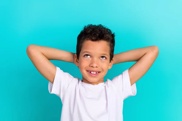 Photo of small positive minded schoolchild hands behind head look up empty space isolated on teal color background.