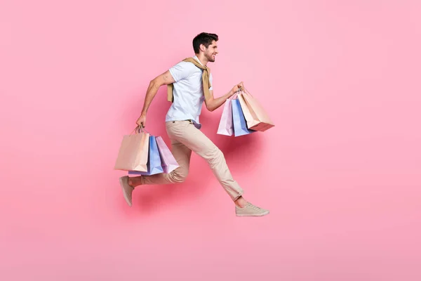Full body profile portrait of crazy guy hold boutique bags jump run empty space isolated on pink color background.