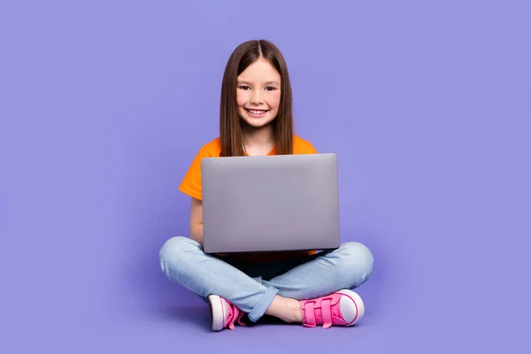 聪明的女学生穿着时髦的T恤衫斜纹棉裤 拿着笔记本电脑 在紫色背景下做家庭作业 — 图库照片