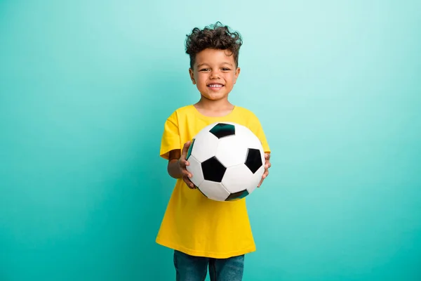 茶色の髪を着た黄色のTシャツが付いているかわいい友好的な学校のボーイの写真はターコイズ色の背景で隔離されたサッカーの球を与えます — ストック写真