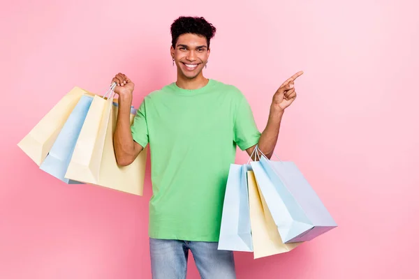 穿着绿色T恤衫的快乐男人拿着购物袋的照片 上面写着在粉色背景上隔离开的空旷空间 — 图库照片