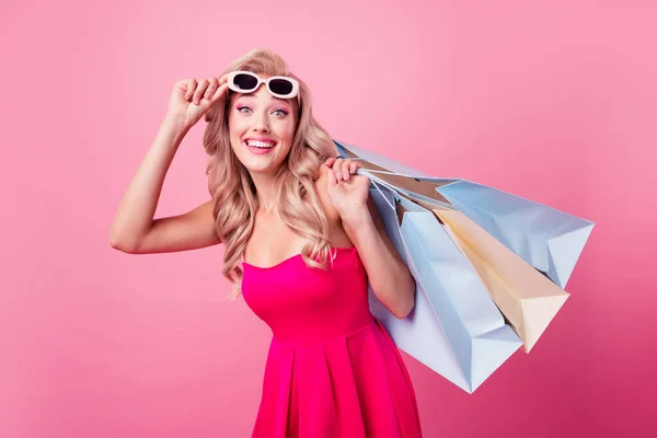 Portrait of pretty excited lady hand hold shopping bags touch sunglass toothy smile isolated on pink color background.