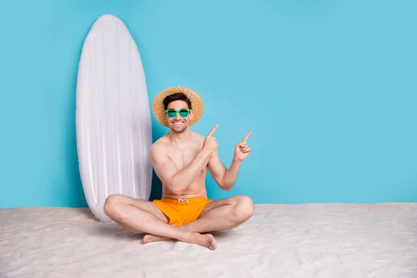 ポジティブクールな男の完全な長さの写真は 空のスペースを指すビーチに座って 青い背景を隔離しました — ストック写真
