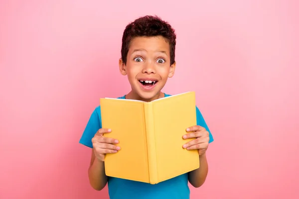 照片上的积极印象深刻的小男孩身穿蓝色T恤 阅读一本有趣的书 书的背景是粉红色的 — 图库照片