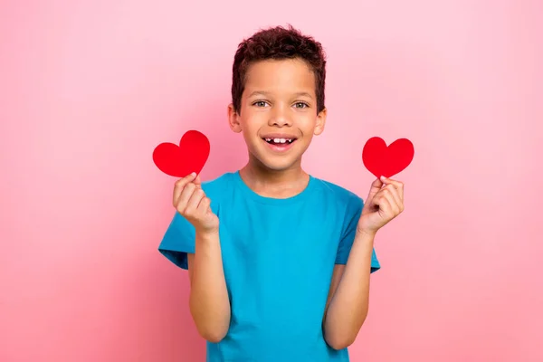 魅力的な小さな男の子の写真の肖像画は ピンク色の背景に隔離されたトレンディなブルーの衣服を2つの赤い心臓ポストカードを保持しています — ストック写真