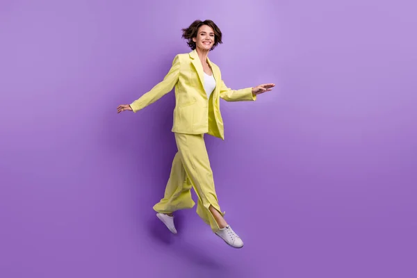 全长照片 兴奋而时髦的女人穿着黄色夹克跳高隔离紫色背景 — 图库照片