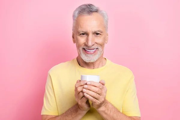 Photo of positive man with gray beard dressed yellow t-shirt hands hold cup of coffee in morning isolated on pink color background.