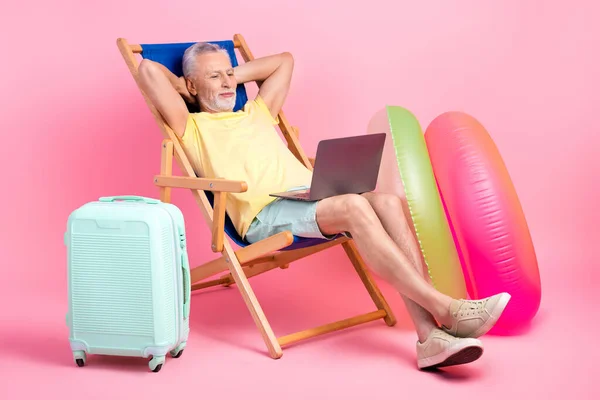 Full body photo of take nap chill pensioner man lying sunbathing chair abroad watch laptop hotel review isolated on pink color background.