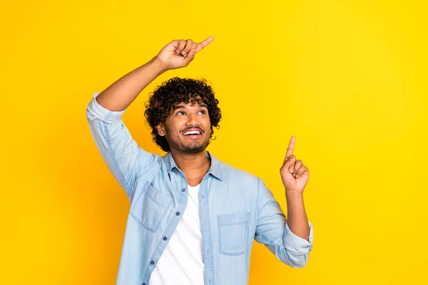 stock image Photo of good mood man with curly hairdo dressed denim shirt directing look at sale empty space isolated on yellow color background.