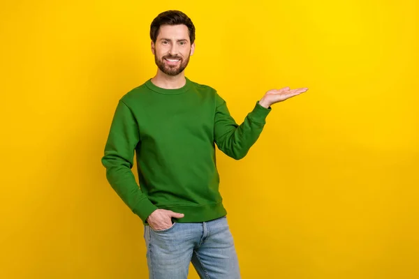 陽気な若いブルネットのビジネスマンの写真は黄色の背景で隔離された腕のウェブサービスの提案を保持する緑のジャンパーを身に着けます — ストック写真