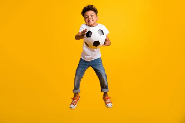 ファンキーな魅力的な小さな男の子の完全な長さの写真は フットボールを隔離された黄色の背景をジャンプする白いTシャツを着用します — ストック写真