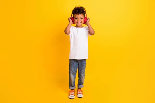 全长照片正面快乐小男孩穿着白色T恤听音乐耳机孤立的黄色背景 — 图库照片