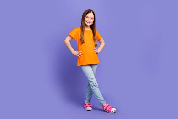 紫色の背景に隔離されたウエストの上にオレンジ色のTシャツのジーンズを着た愛らしいクールな子供の完全な長さの写真 — ストック写真