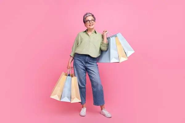 Full length photo of minded positive lady hold store mall bags look empty space ad isolated on pink color background.