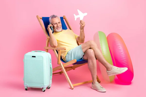 Full body cadre of cheerful satisfied relax pensioner man holding paper airplane call his tour operator isolated on pink color background.