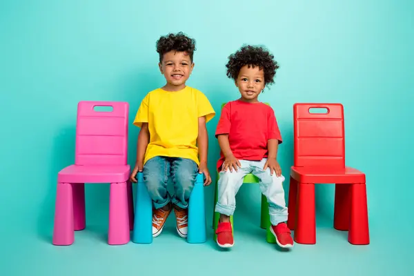 两个可爱的小男孩朋友坐在椅子上 穿着时髦的衣服 背景是青色的 — 图库照片