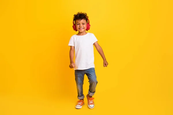 ファンキーな陽気な小さな男の子の完全な長さの写真 白いTシャツを着たウォーキング 楽曲イヤホン隔離された黄色の背景 — ストック写真