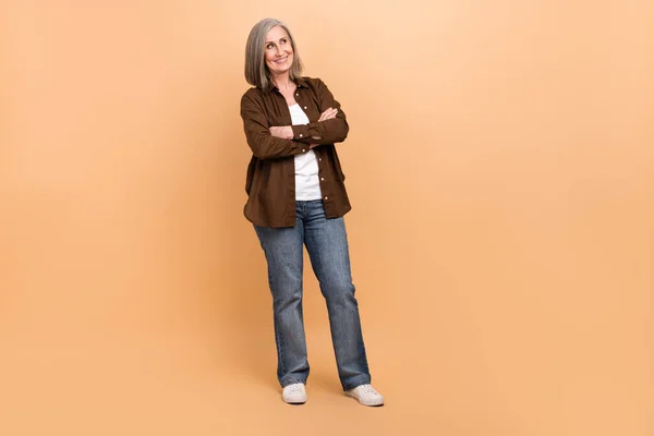 Full length body cadre of thoughtful mature age woman folded arms looking empty space creative idea isolated on beige color background.